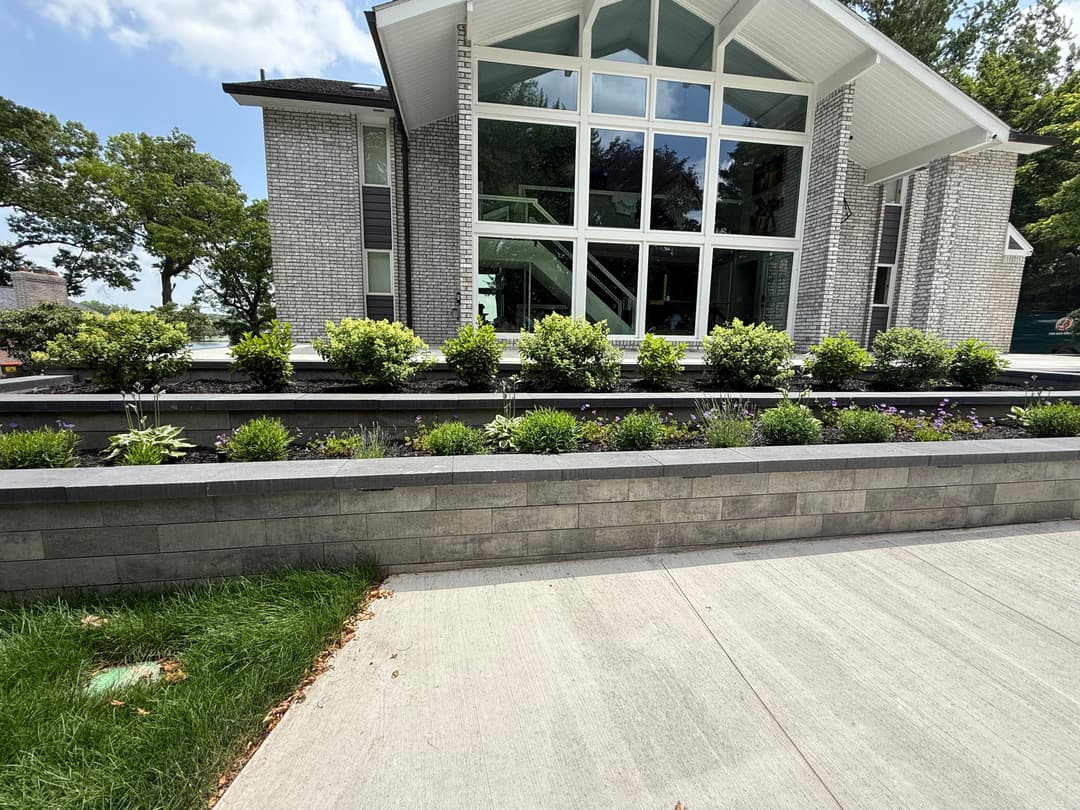 Modern home exterior with large windows, landscaped garden, and stone retaining wall.
