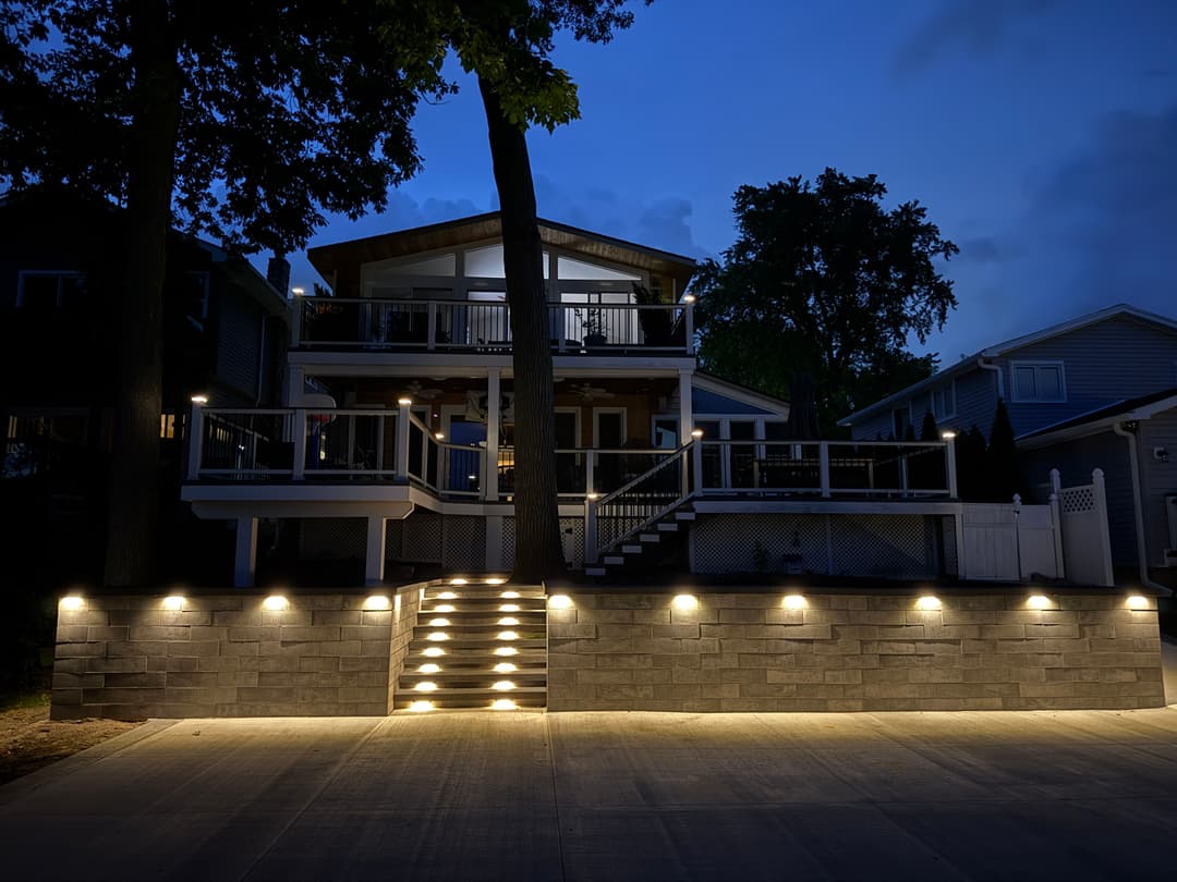 Modern two-story lakeside house illuminated by outdoor lights at dusk.