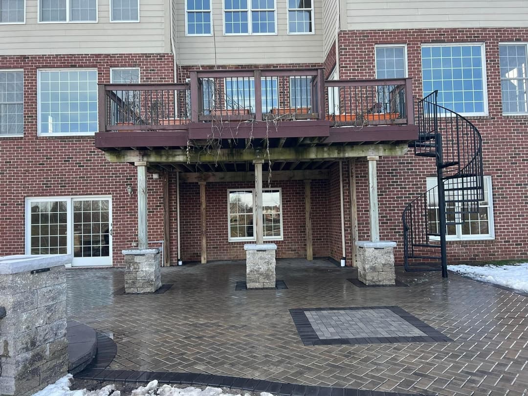 Spacious brick patio with spiral staircase and elevated deck in a residential setting.