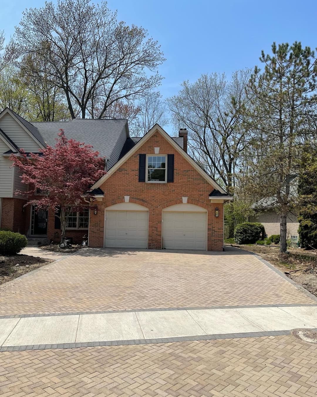 Brick house with double garage, landscaped yard, and sunny blue sky.