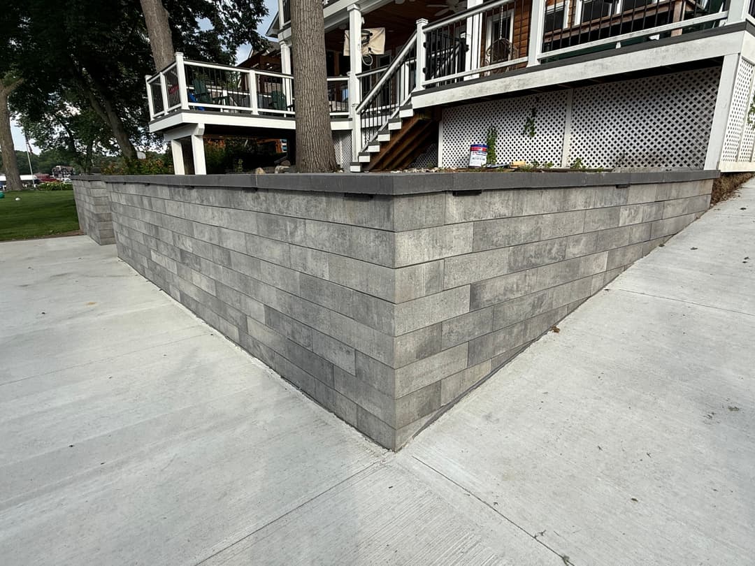 Gray stone retaining wall alongside a concrete path near a house with a deck.