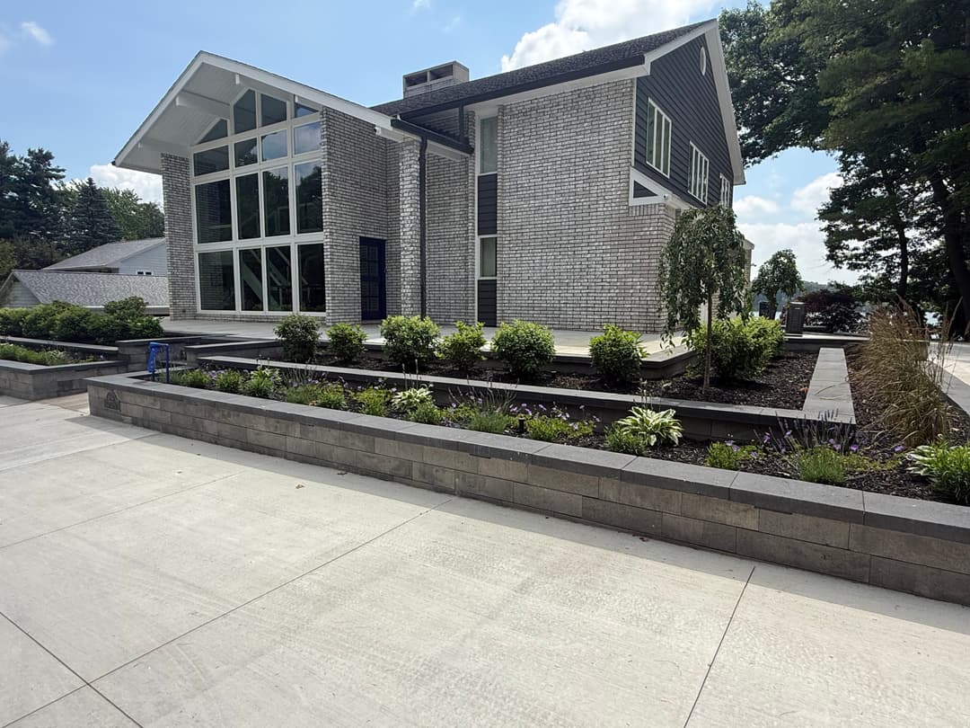 Modern house with large windows, landscaped gardens, and sleek concrete pathway.