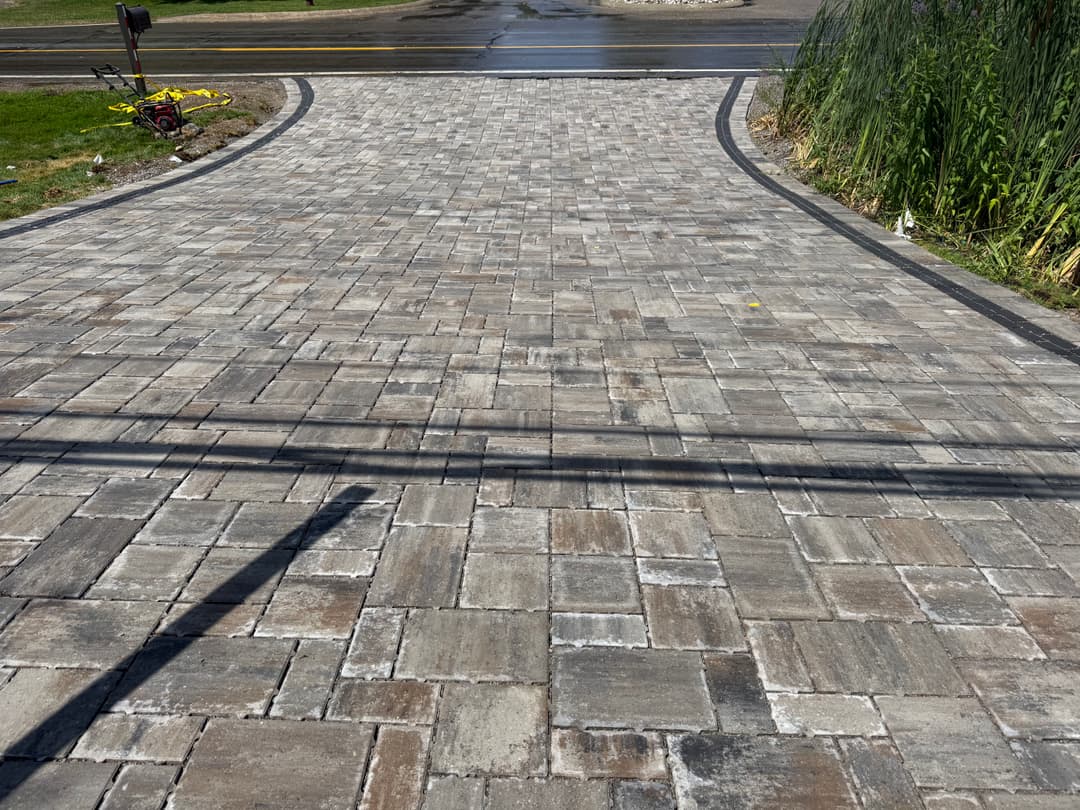 Paved driveway with interlocking stones, showing a curving design and surrounding greenery.
