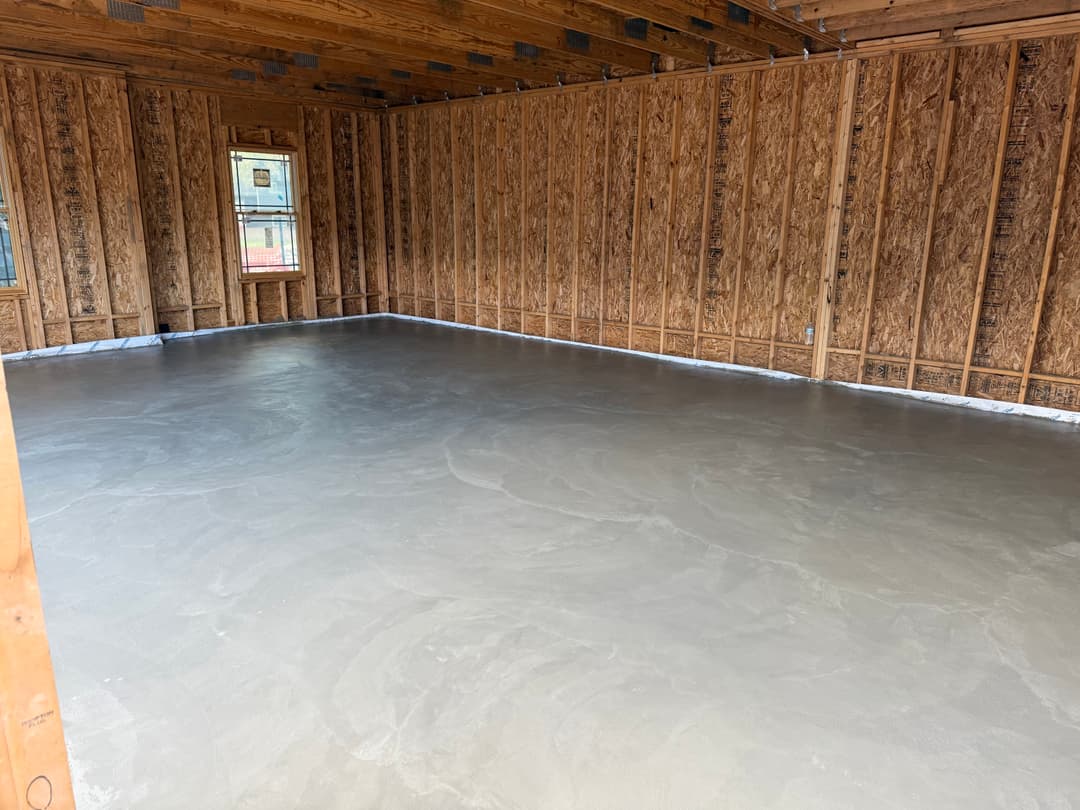 Newly poured concrete floor in an unfinished room with wooden walls and a window.