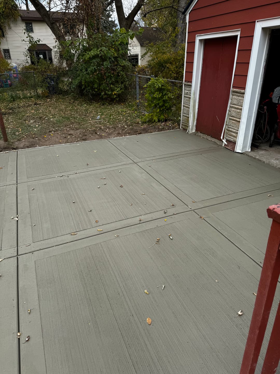 Freshly poured concrete driveway adjacent to a red garage with autumn leaves scattered.