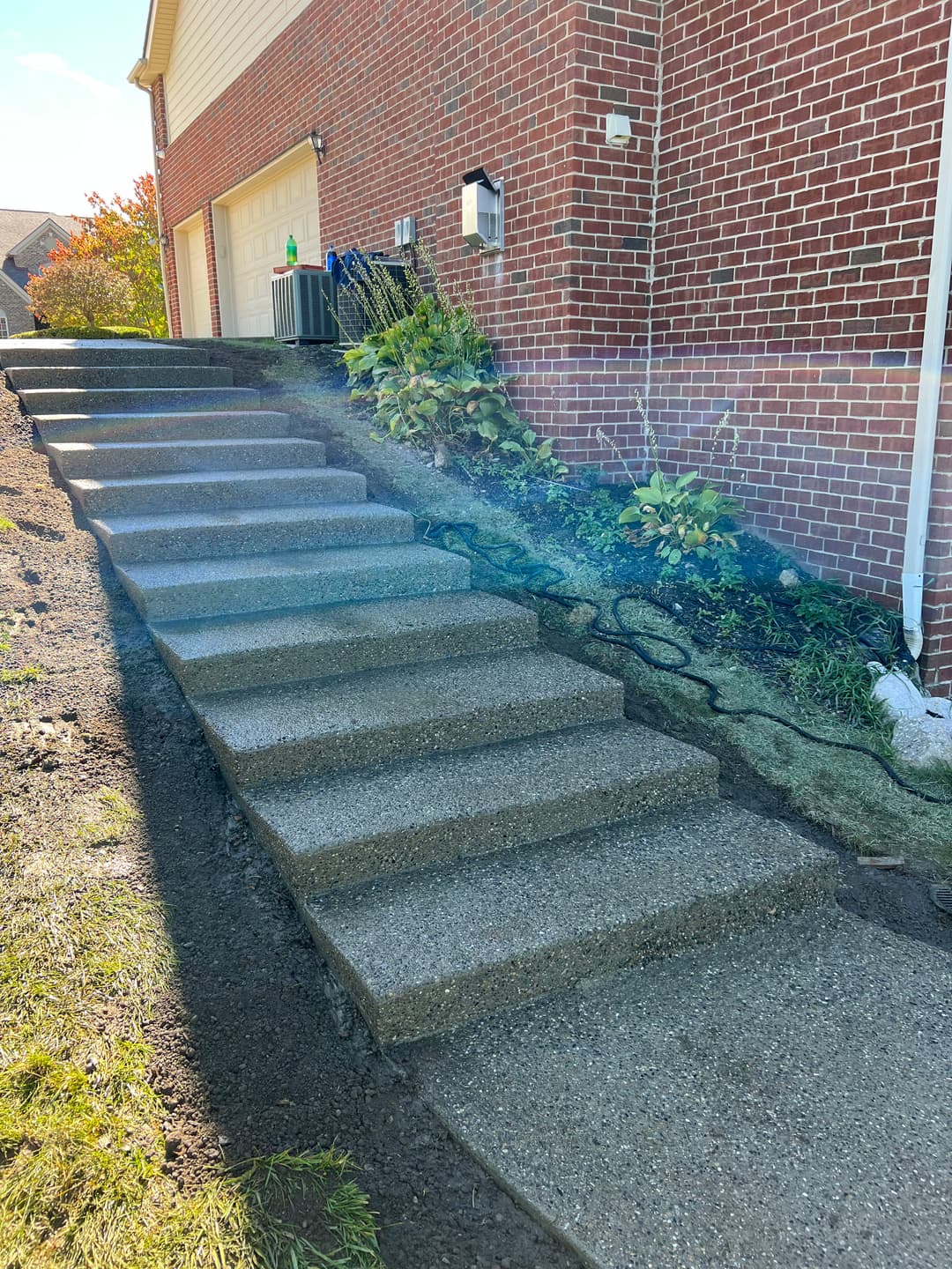 Concrete steps leading to a home, with landscaping and brick wall in the background.