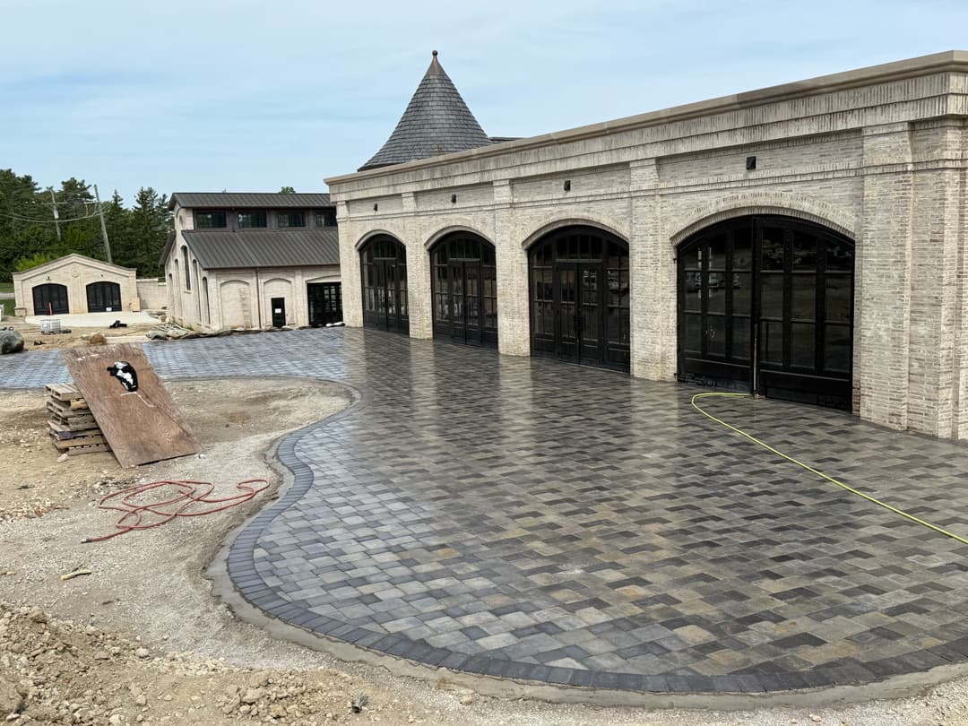 Paved patio with stone bricks outside a building under construction, surrounded by landscaping.