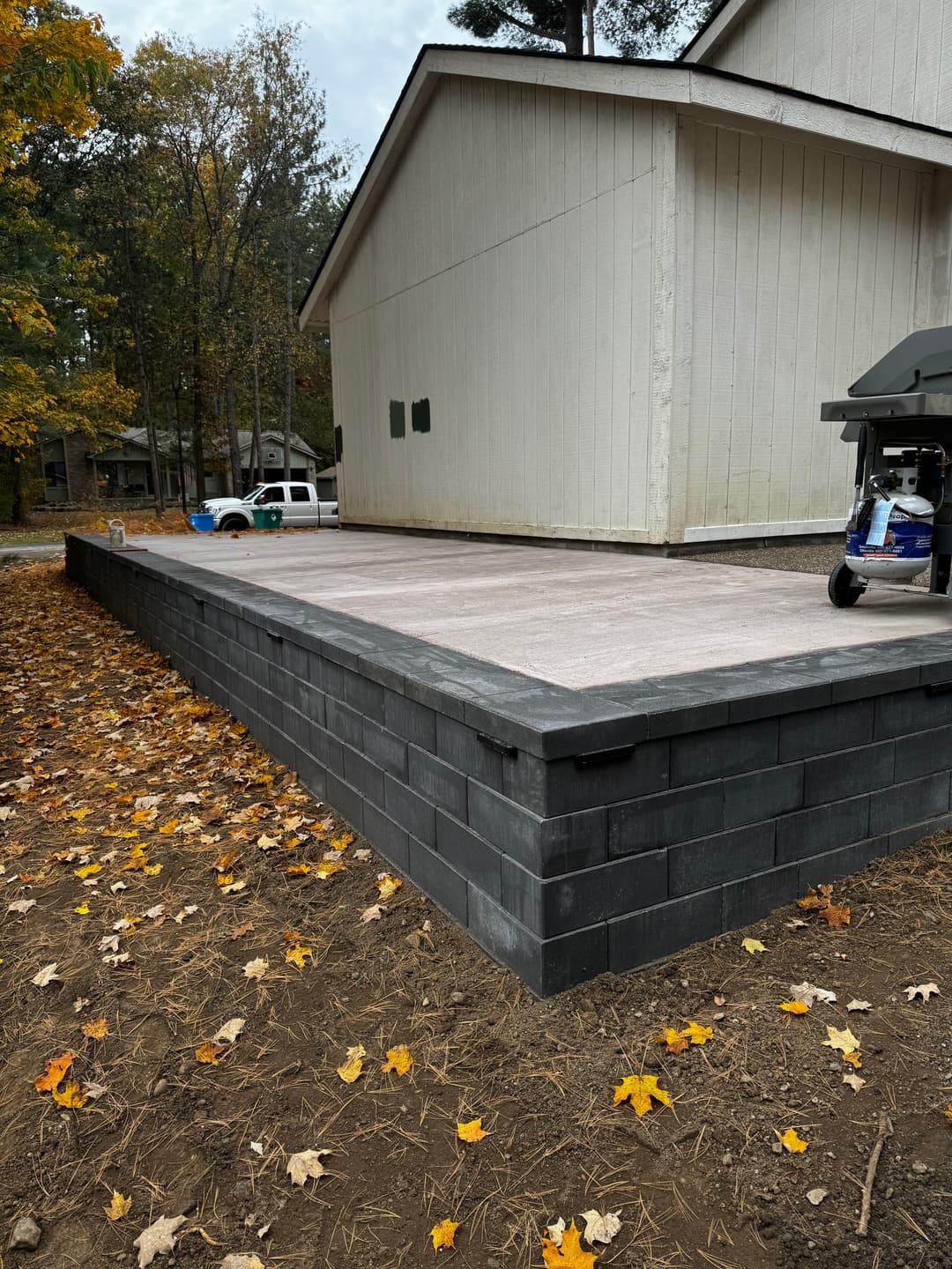 Paved patio with stone wall in autumn landscape near a house.