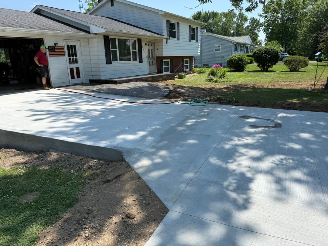 Newly poured concrete driveway leading to a suburban home with landscaping and a garage.