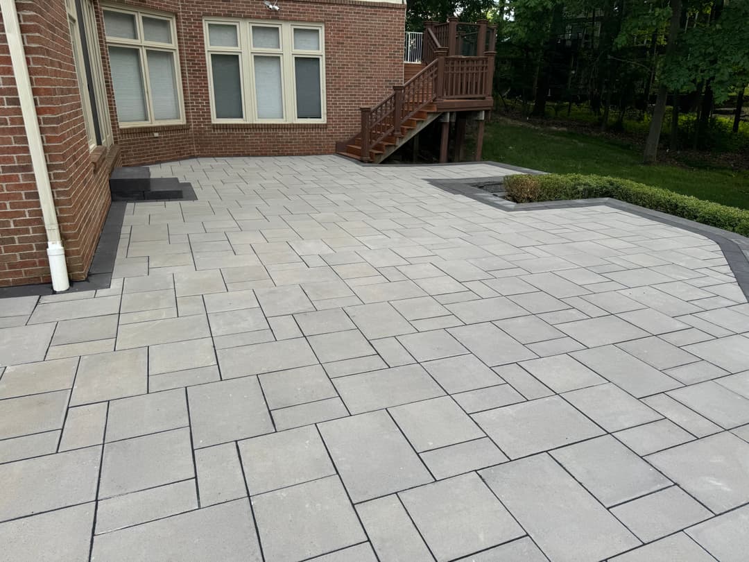 Paved outdoor patio with gray stone tiles and a wooden deck in a landscaped backyard.