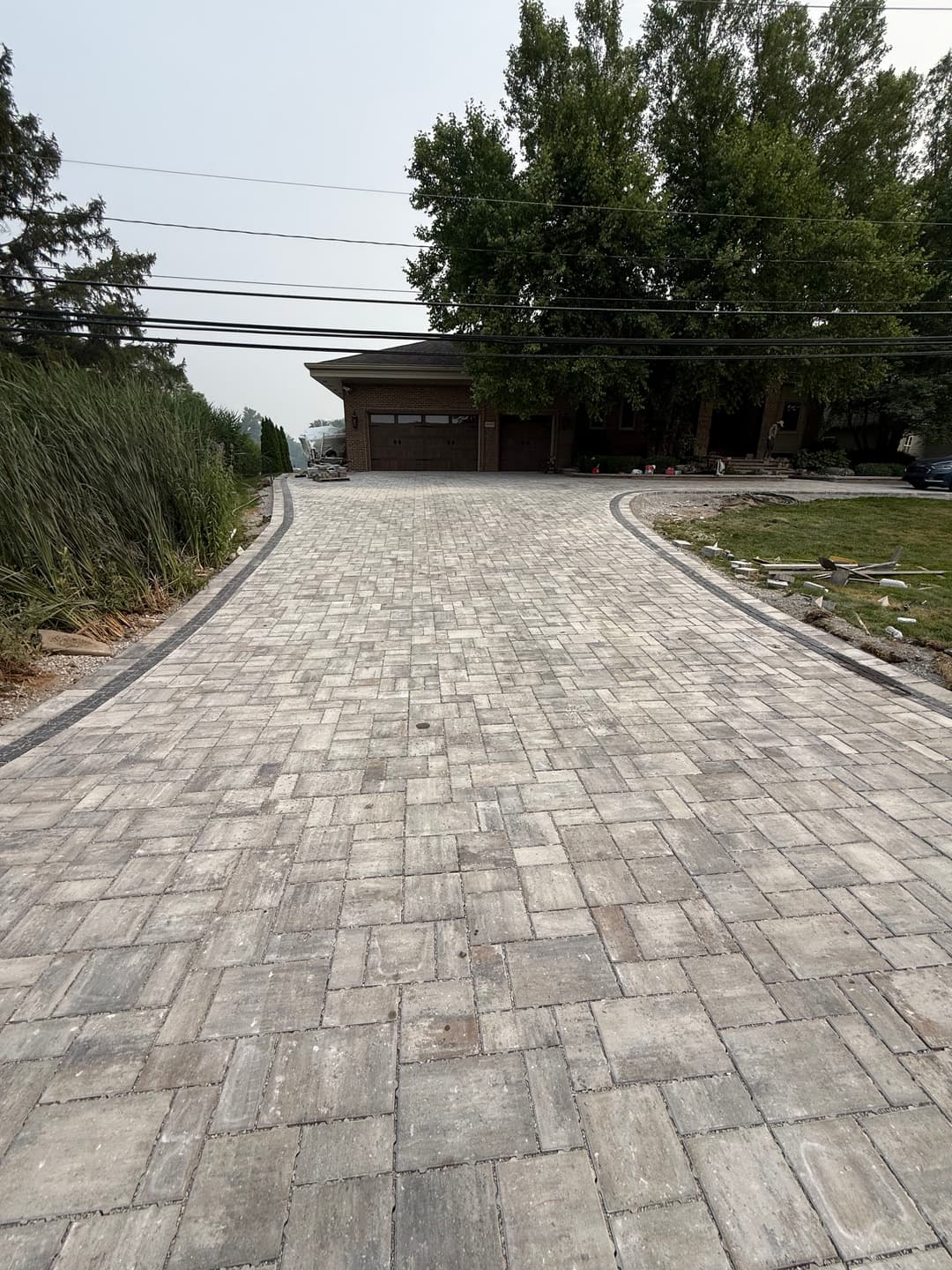 Paved stone driveway leading to a home surrounded by trees and grass.
