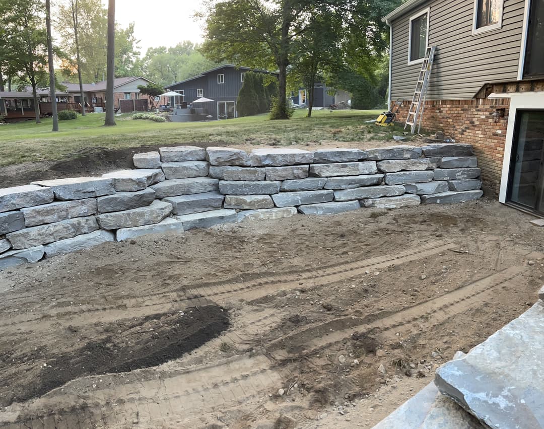 Stone wall construction in a backyard with earthwork and landscaping underway.