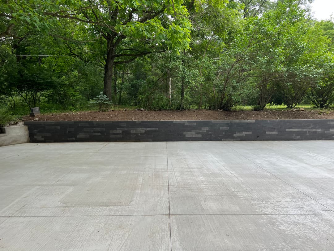 Concrete driveway with a landscaped area and greenery in the background.
