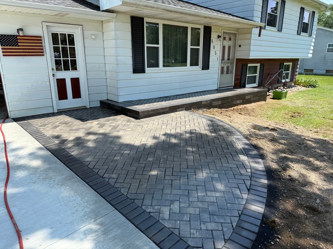 Paver stone walkway and steps leading to a white house with American flag.