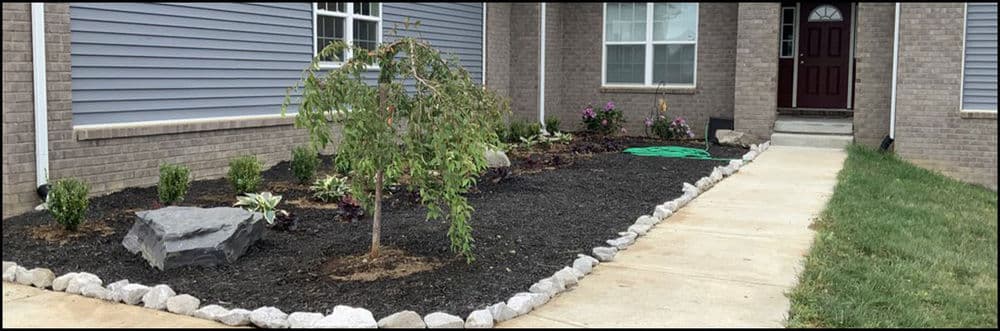 Landscaped front yard with rocks, plants, and a walkway leading to a doorway.