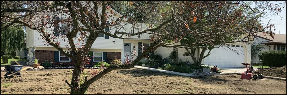 Front yard landscaping project with freshly turned soil, home, and tools visible.