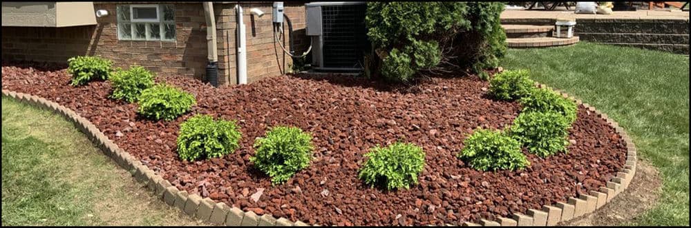 Landscape design with red rock mulch and green shrubbery in a residential yard.