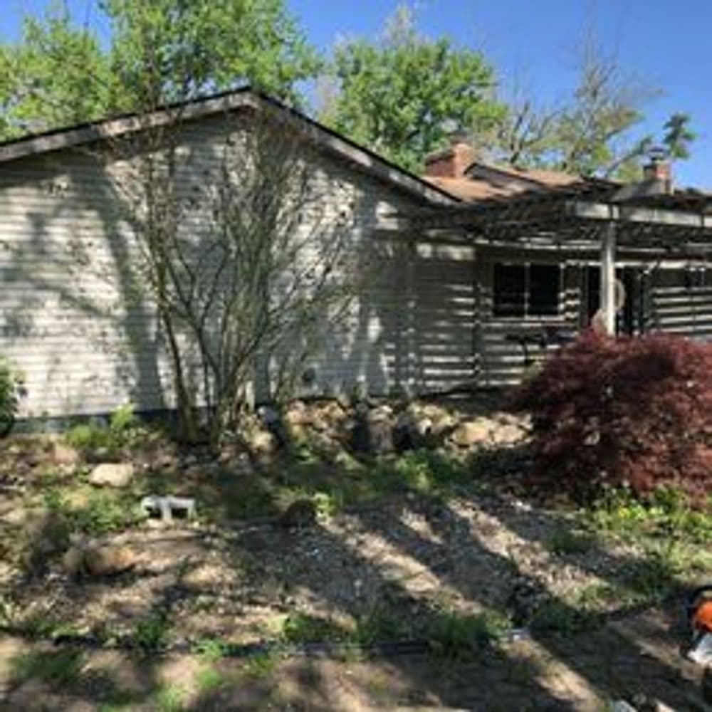 Front view of a residential house with a garden and trees in a suburban setting.