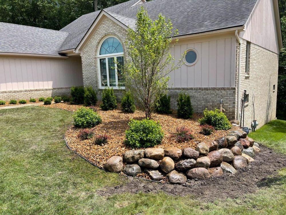 Landscaped home exterior with shrubs, decorative rocks, and a young tree near the entrance.