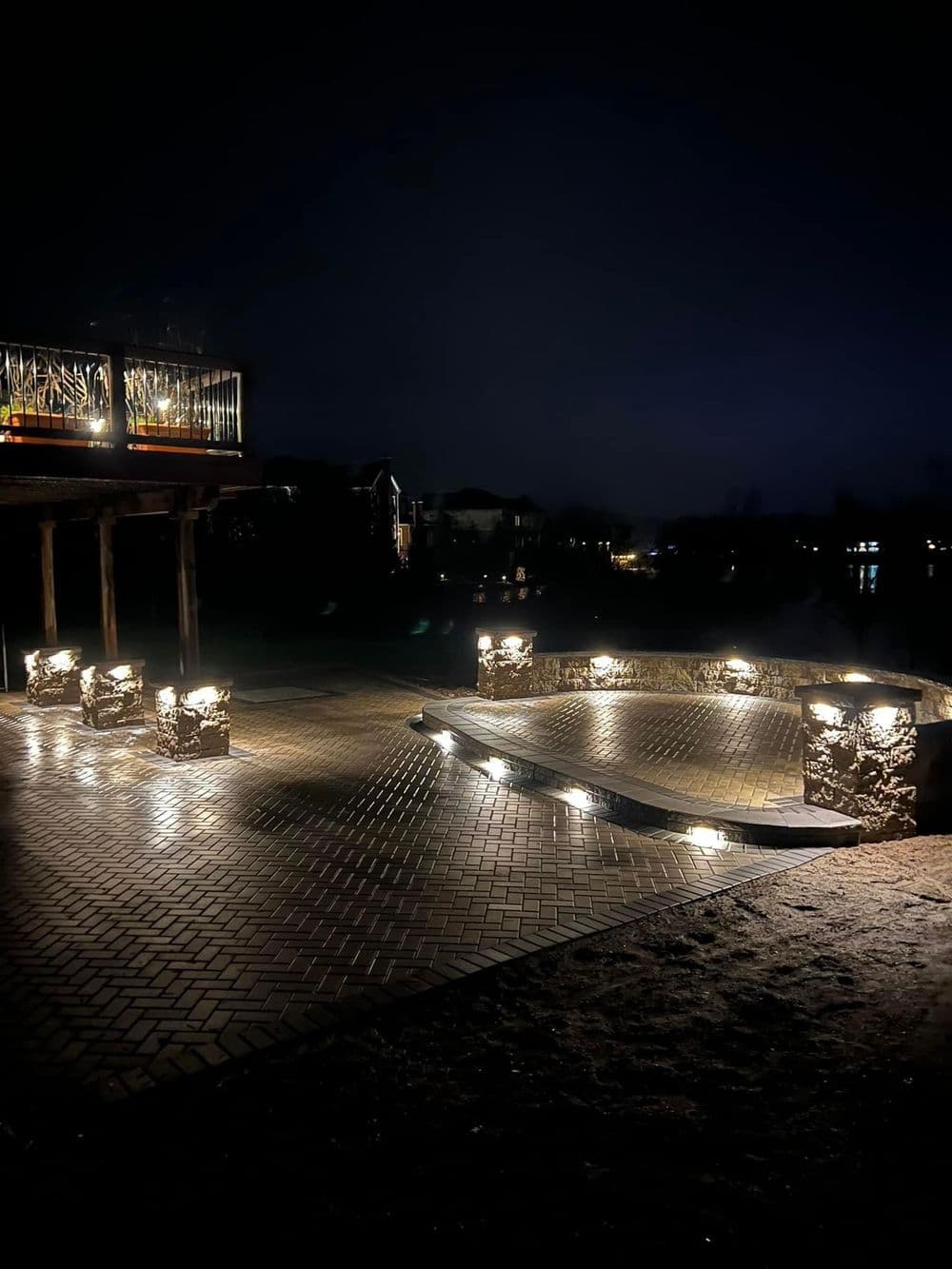 Illuminated outdoor patio with stone lighting and a deck overlooking a dark lake.
