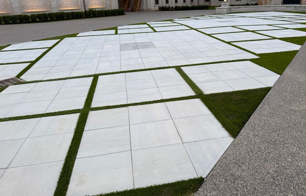 Modern outdoor patio design featuring large tiles and green grass patches.